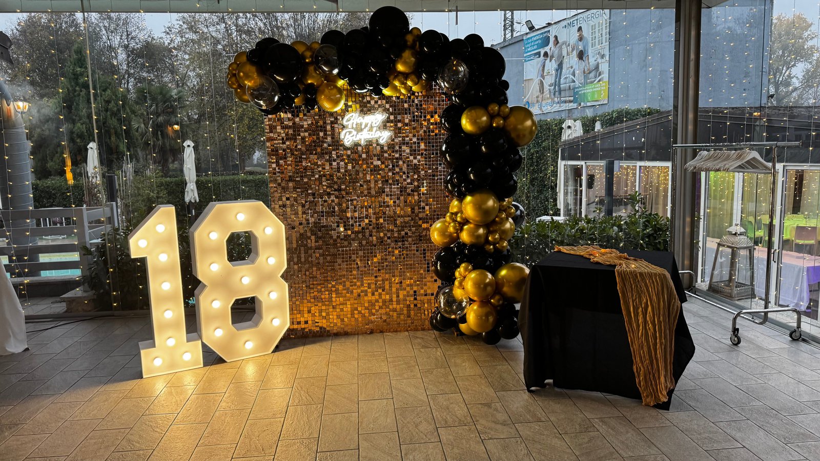 18esimo compleanno con palloncini oro e neri, parete paillettes dorata e numeri luminosi 18